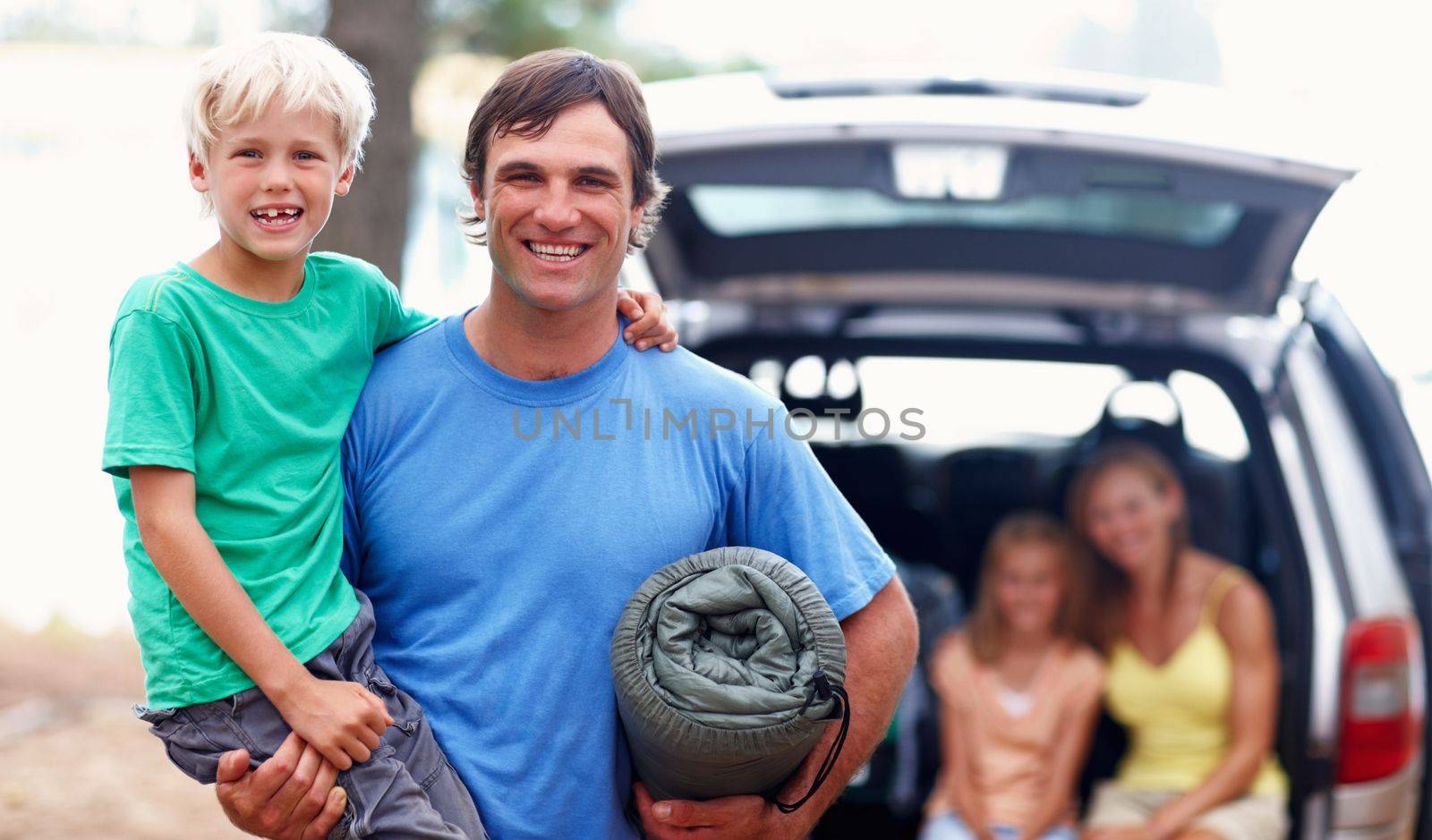 Father carrying son. Portrait of father carrying son and smiling with family sitting in car. by YuriArcurs