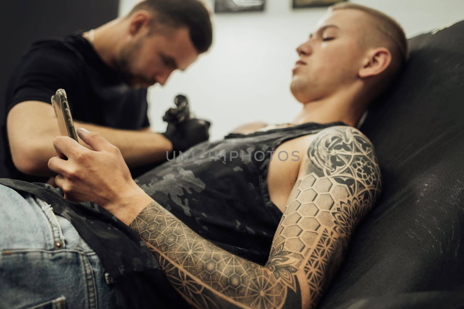 Tattooed Man Using Smartphone During Tattoo Session, Male Artist Draws on Clients Skin