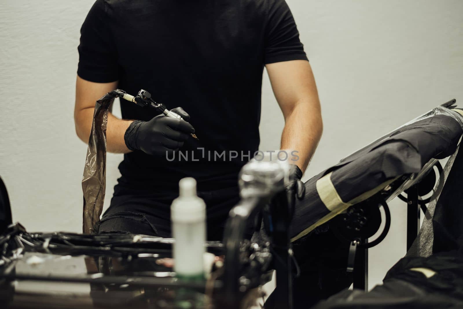 Male Tattoo Artist Holds Tattoo Machine While Sitting on His Workplace at the Studio by Romvy