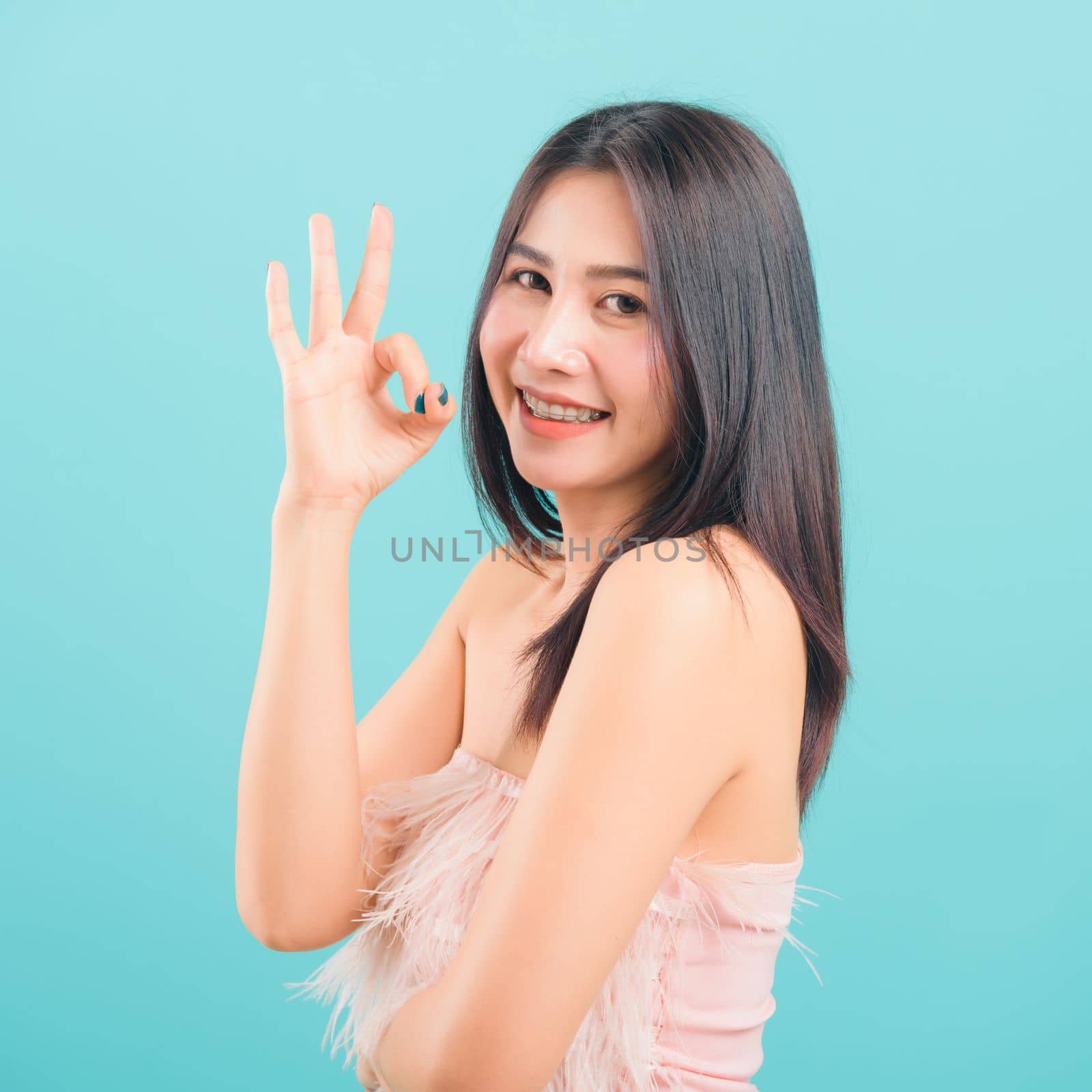 Portrait asian beautiful woman smiling showing finger OK sign and her looking to camera on blue background, with copy space for text