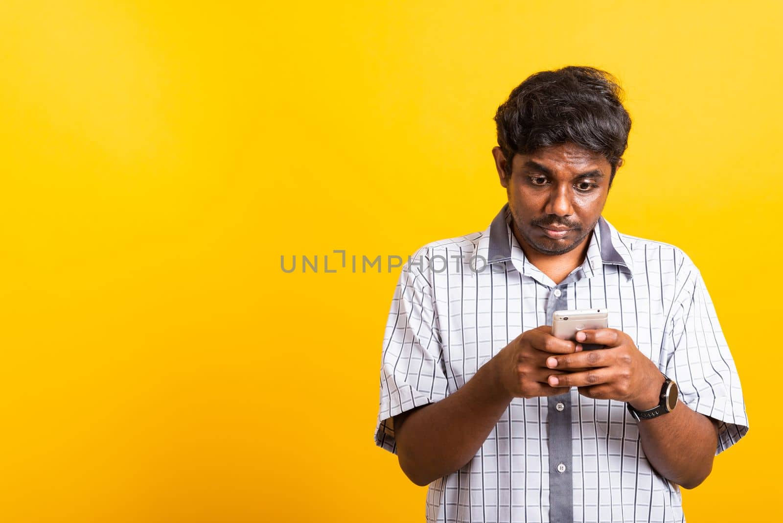 Asian happy portrait young black man smile standing wear shirt making typing or reading social message on mobile smart phone blank screen isolated, studio shot yellow background with copy space