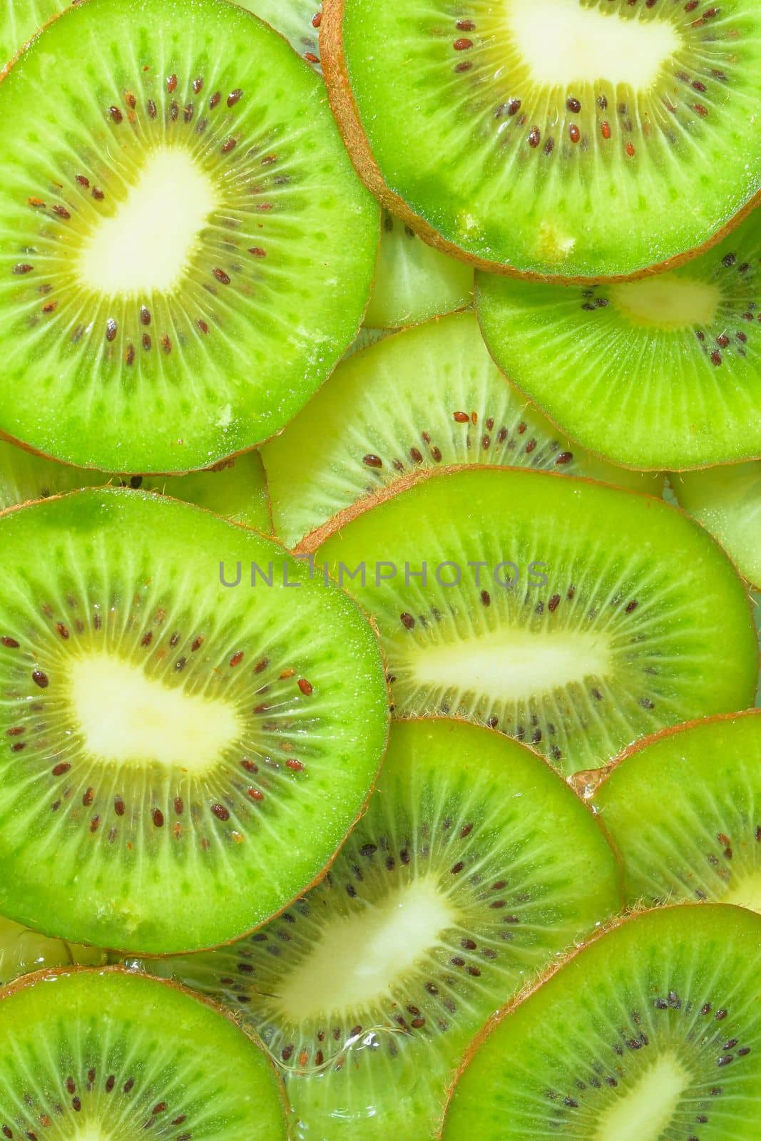 Close-up view of the green kiwi fruit slices in water background. Texture of cooling fruit drink with macro bubbles on the glass wall. Flat design. Vertical image by roman_nerud