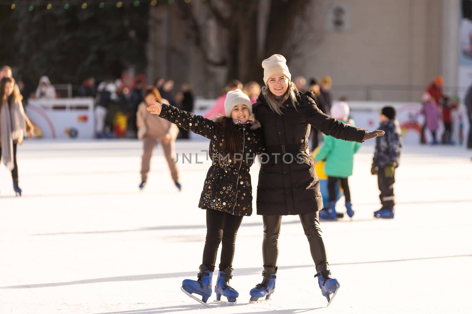 beautiful happy mother and daughter smiling at camera while standing together on skating rink