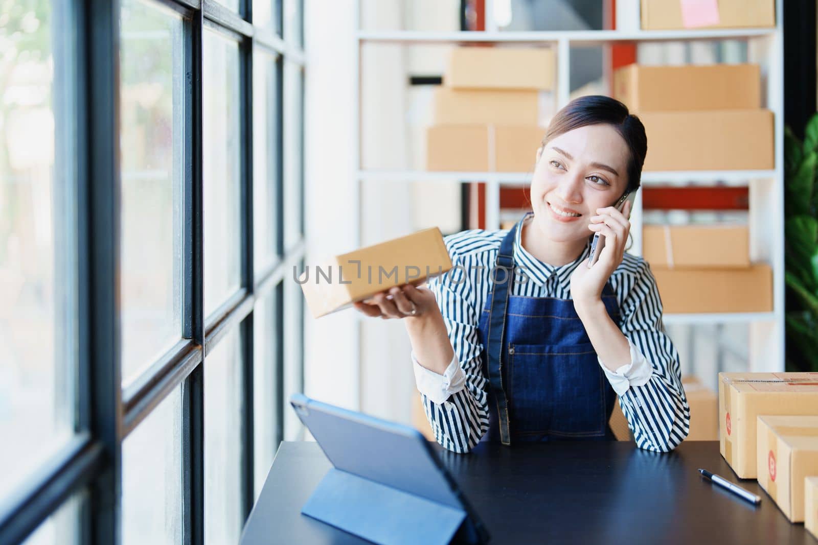 Starting small business entrepreneur of independent Asian female online seller talking on the phone with a customer and packing products for delivery to the customer. and SME delivery concept.