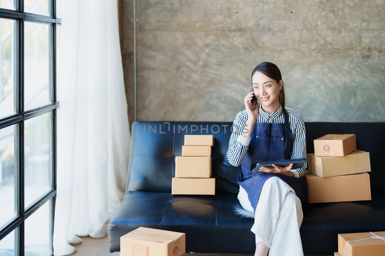 Starting small business entrepreneur of independent Asian female online seller talking on the phone with a customer and packing products for delivery to the customer. and SME delivery concept.