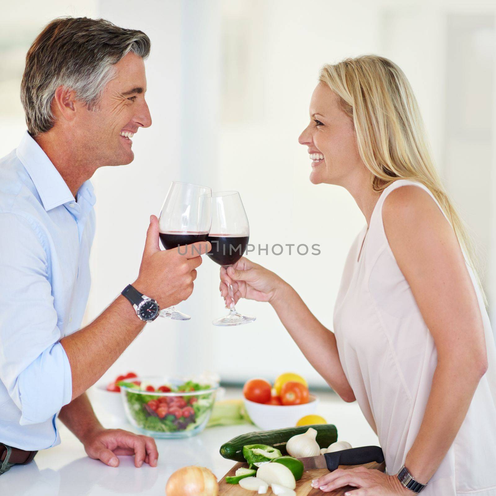 Heres to us and a wonderful life. an affectionate couple toasting with red wine while making dinner