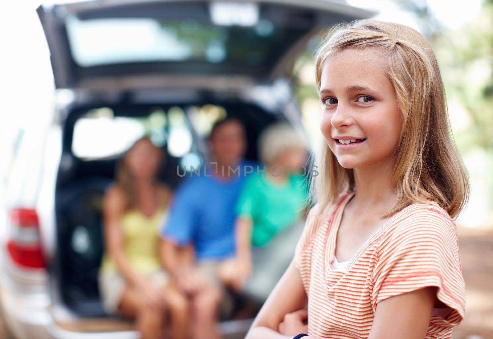 Pretty young girl smiling. Portrait of pretty young girl standing with hands folded and family sitting in the back of a car