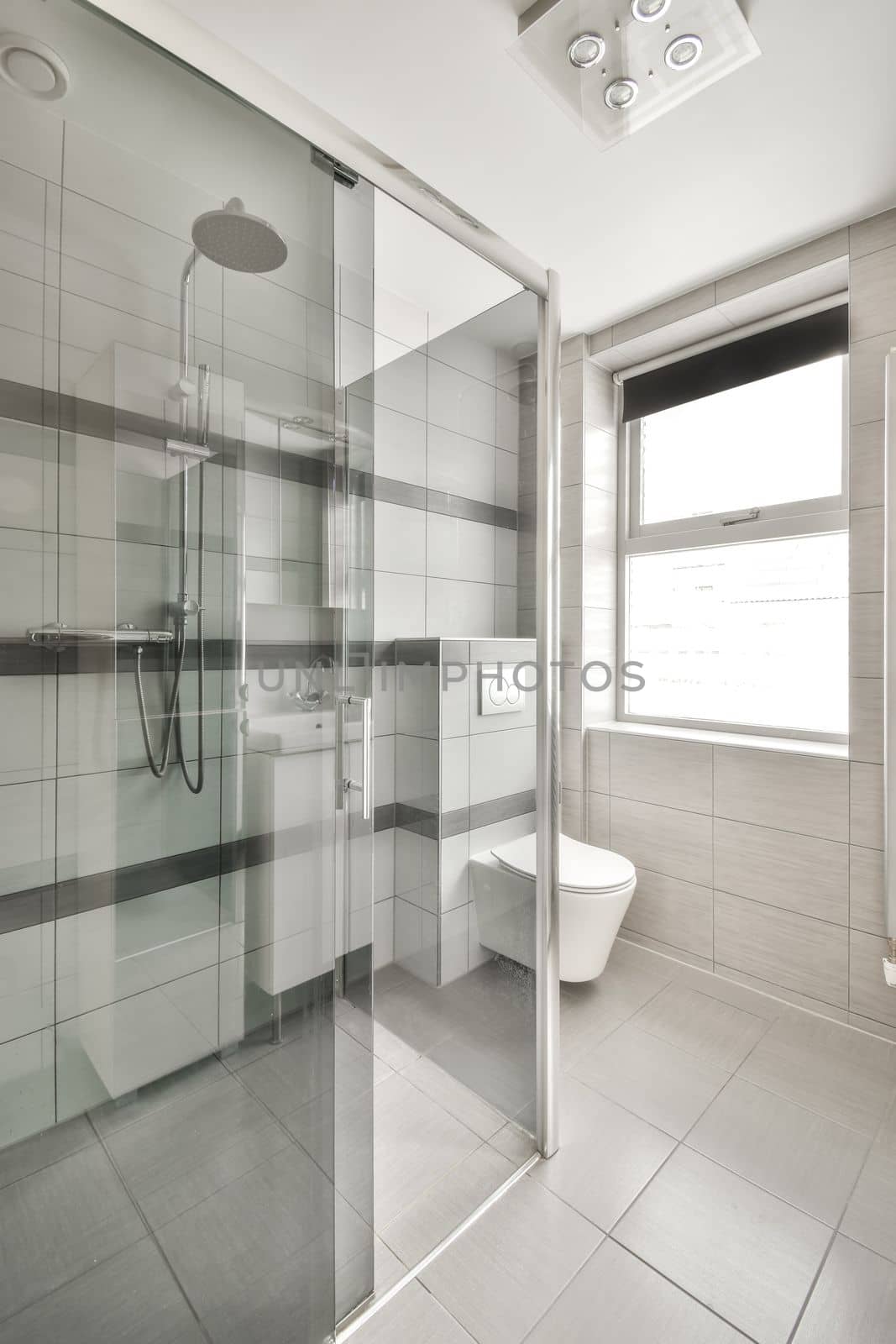 a modern bathroom with white and gray tiles on the walls, glass shower stall and toilet in the middle part of the room