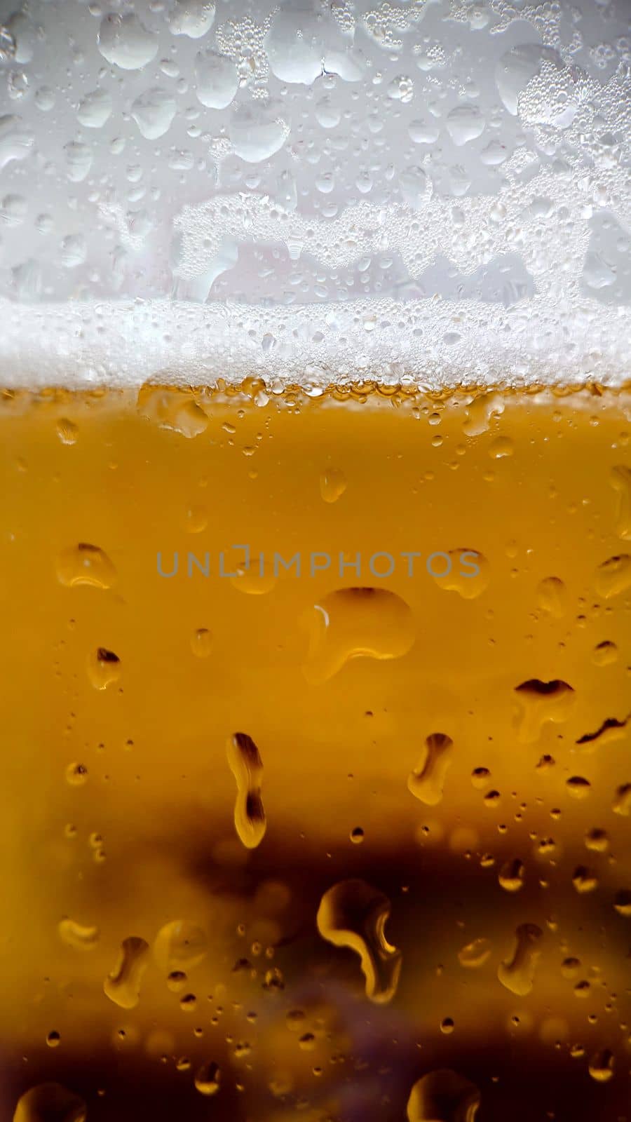 White foam and condensation drops on the walls of a glass of chilled beer.Texture or background.Macrophotography.