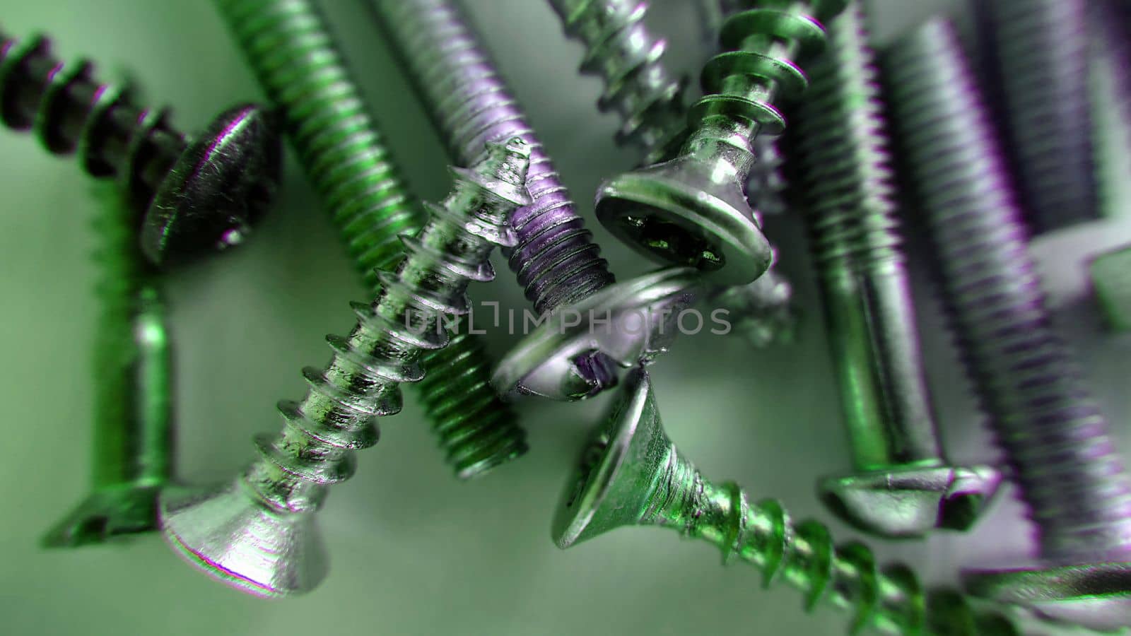 Screws bolts of different sizes randomly lie on the table and are highlighted in green . Macrophotography.Texture or background.Selective focus.