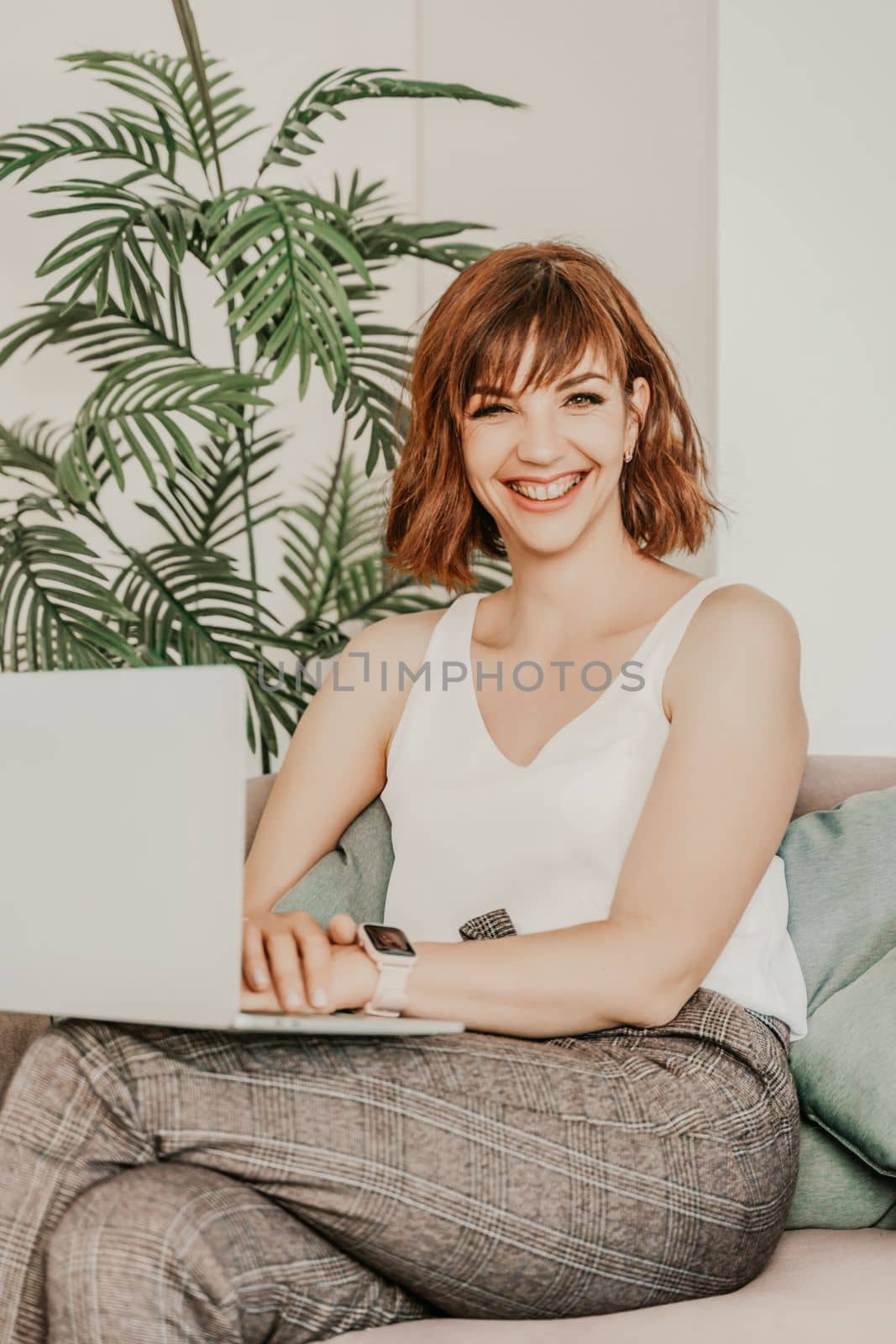 Attractive young asian woman using laptop computer while sitting on a couch at home by Matiunina