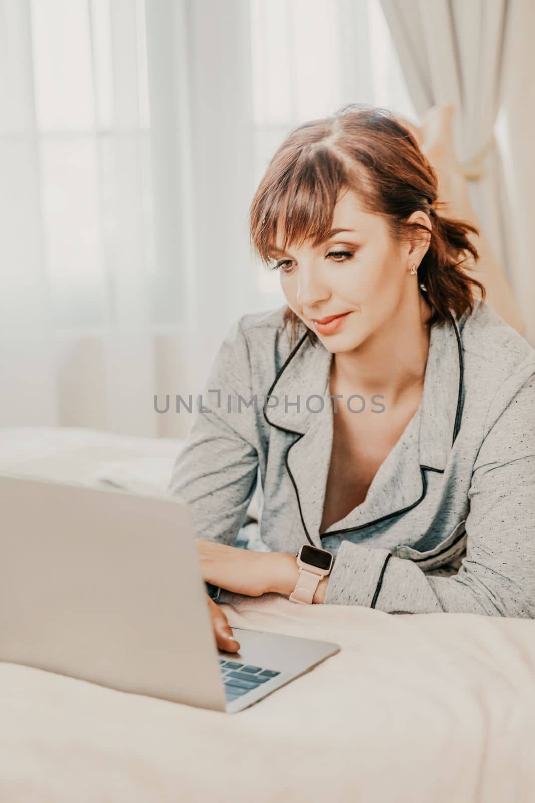 Freelancer woman wears pajamas, she lies in bed and uses work on laptop, computer, study on the Internet, surf the internet, relax, relax, spend time in the bedroom, living room, at home, in the hotel room, wake up