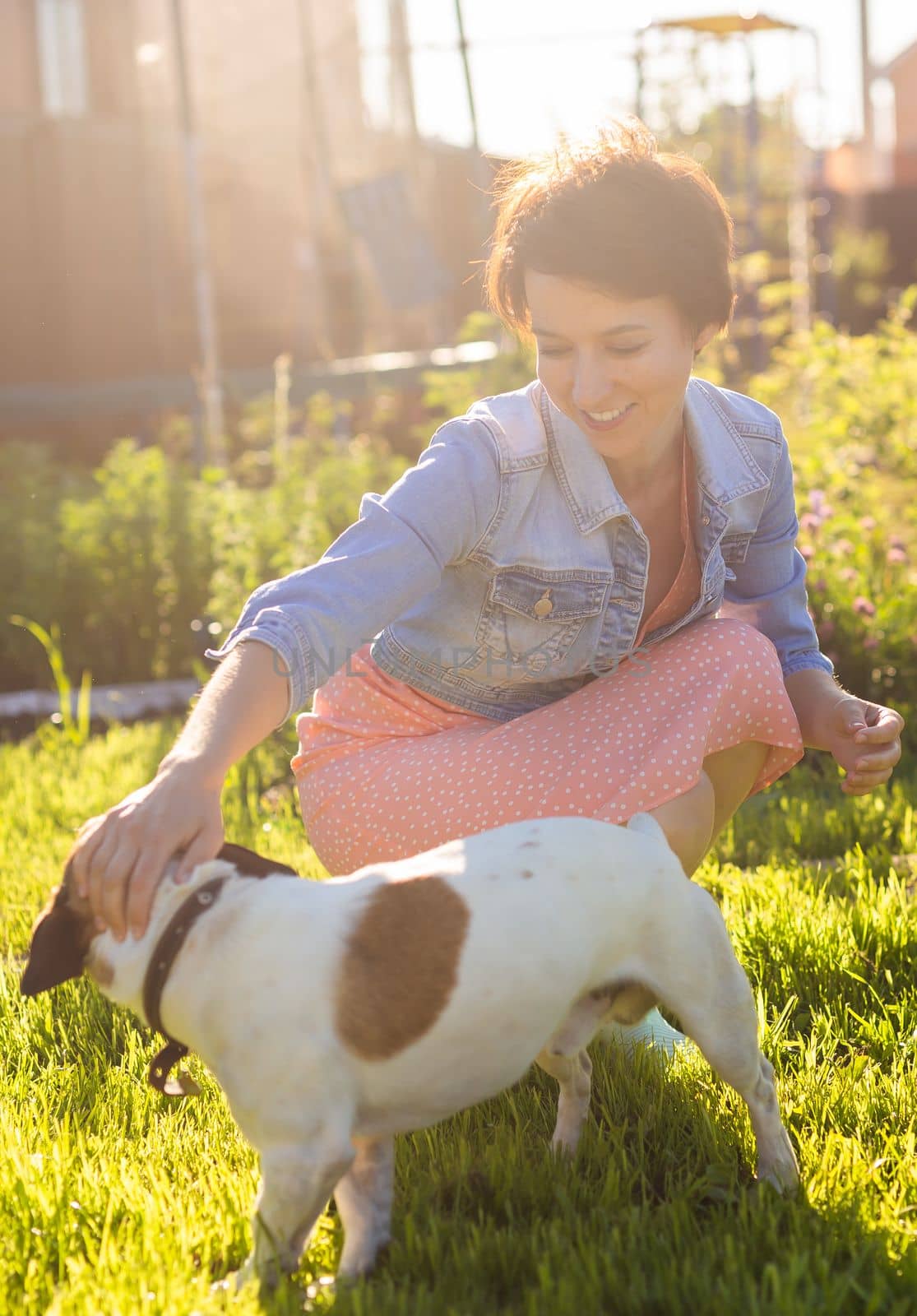 Young woman plays with her dog on the grass on backyard. The concept of animals and friendship or pet owner and love.