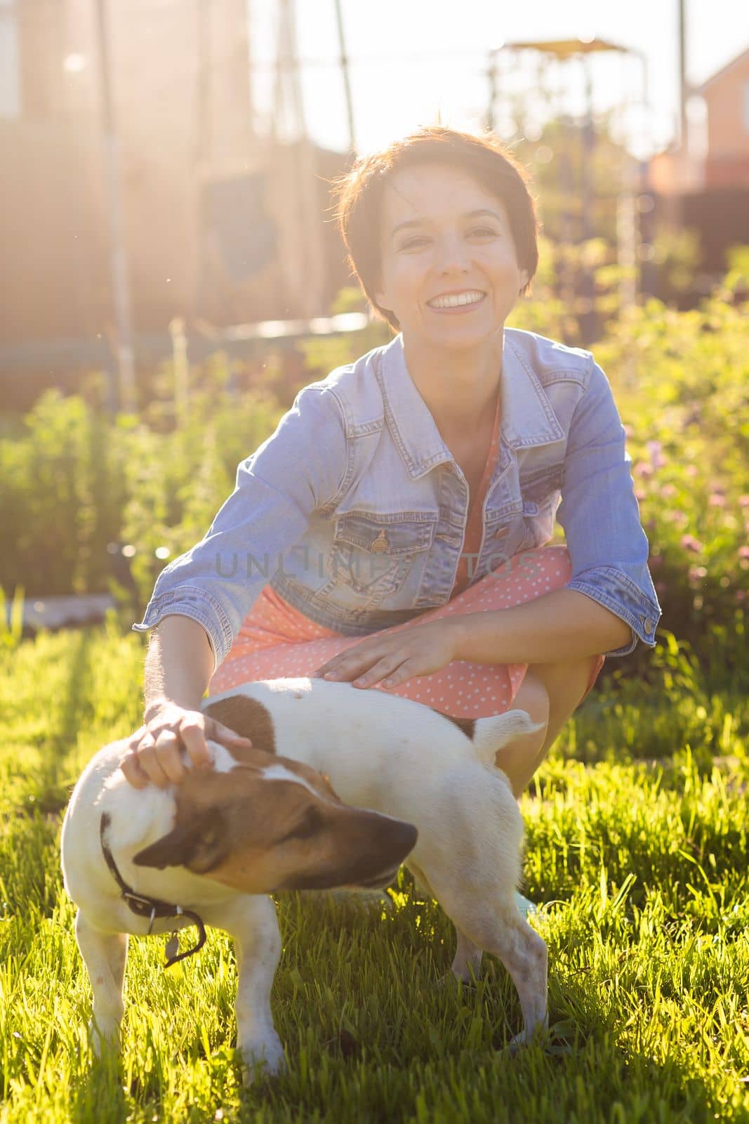 Young woman plays with her dog on the grass on backyard. The concept of animals and friendship or pet owner and love by Satura86