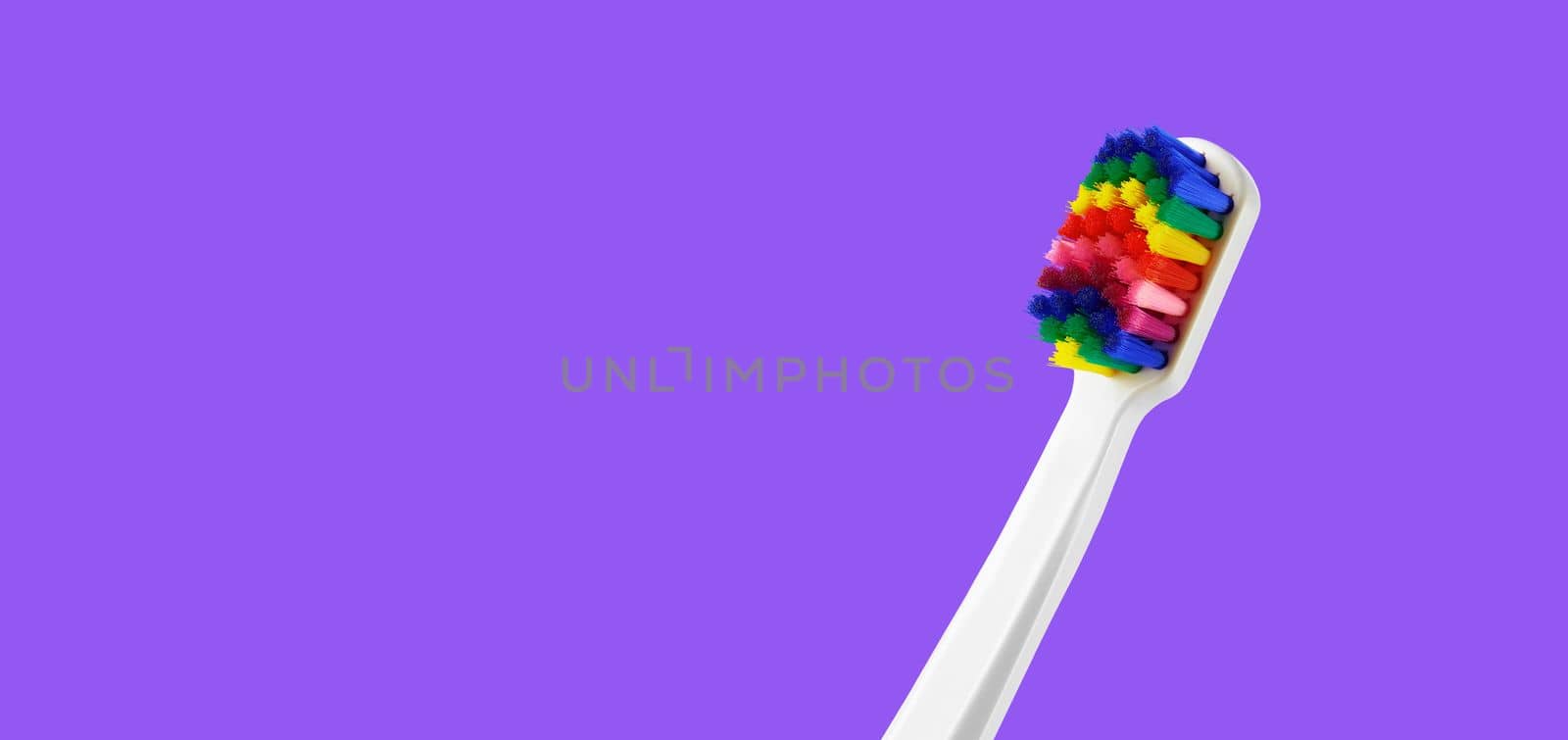 White toothbrush with multicolored bristles on royal purple background. Bristles in all colors of the rainbow. Rainbow toothbrush with white knob. Fashionable oral care by EvgeniyQW