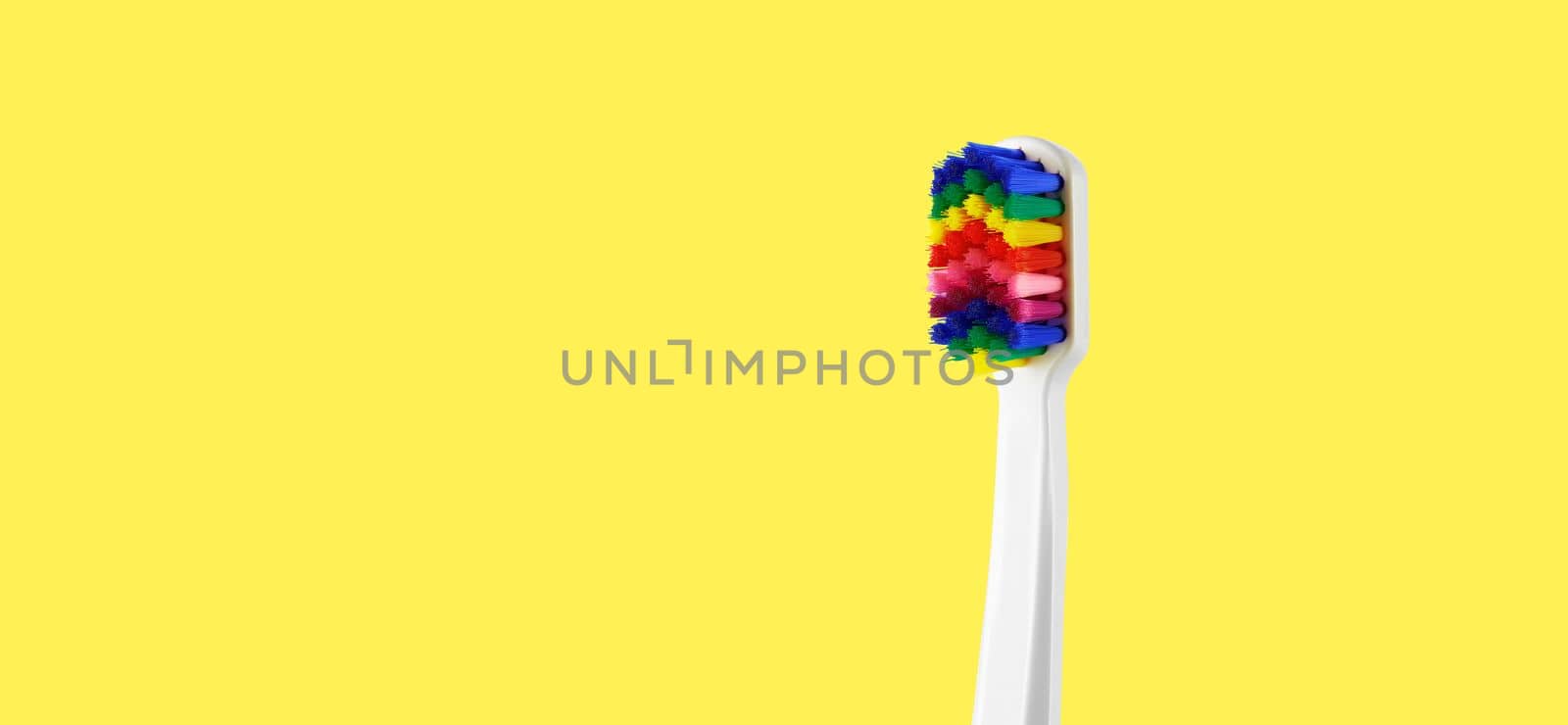 White toothbrush with multicolored bristles on yellow background. Bristles in all colors of the rainbow. Rainbow toothbrush with white knob. Fashionable oral care by EvgeniyQW
