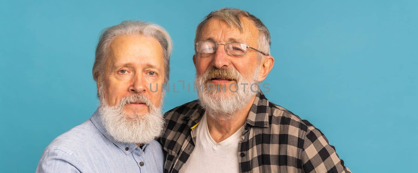 Portrait two elderly man friends standing over blue background - friendship, aged and senior