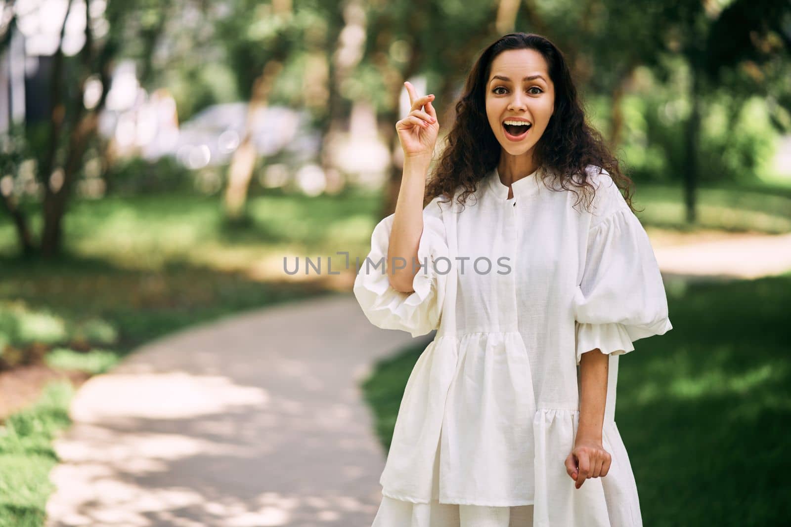 Cheerful curly-haired brunette girl with open mouth raises her index finger. Girl has an idea. High quality photo