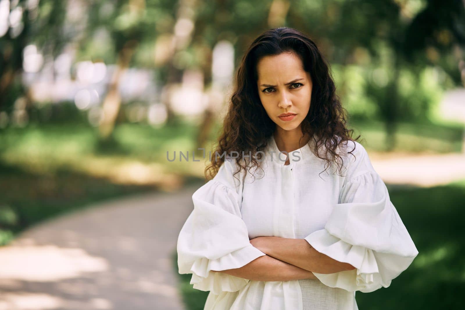 Angry emotions of a curly-haired brunette girl with crossed arms in the park. High quality photo