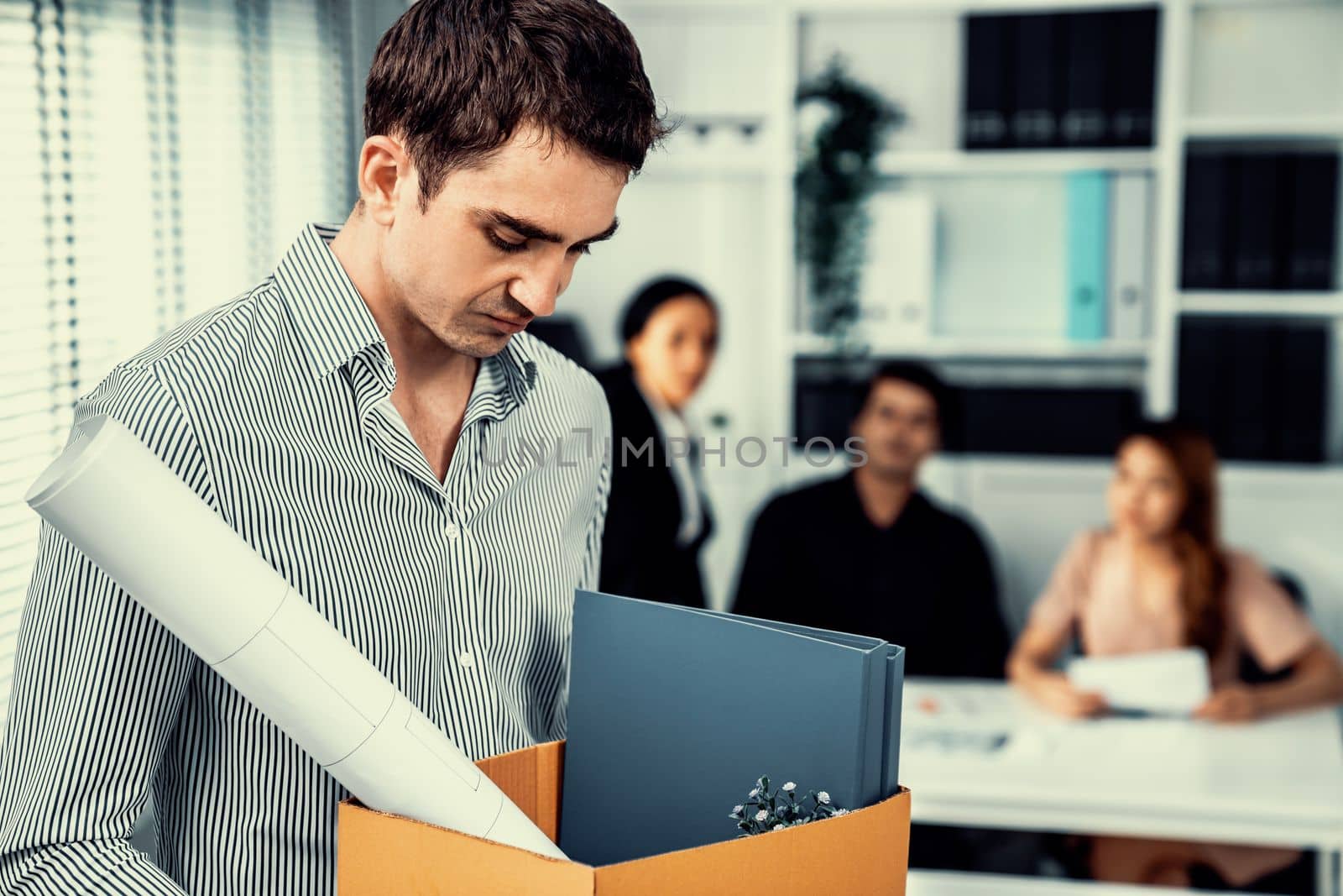 Depressed and disappointed employee packing his belongings after being fired for not being competent. Gossiped by his colleagues behind his back. Layoff due to economic depression.