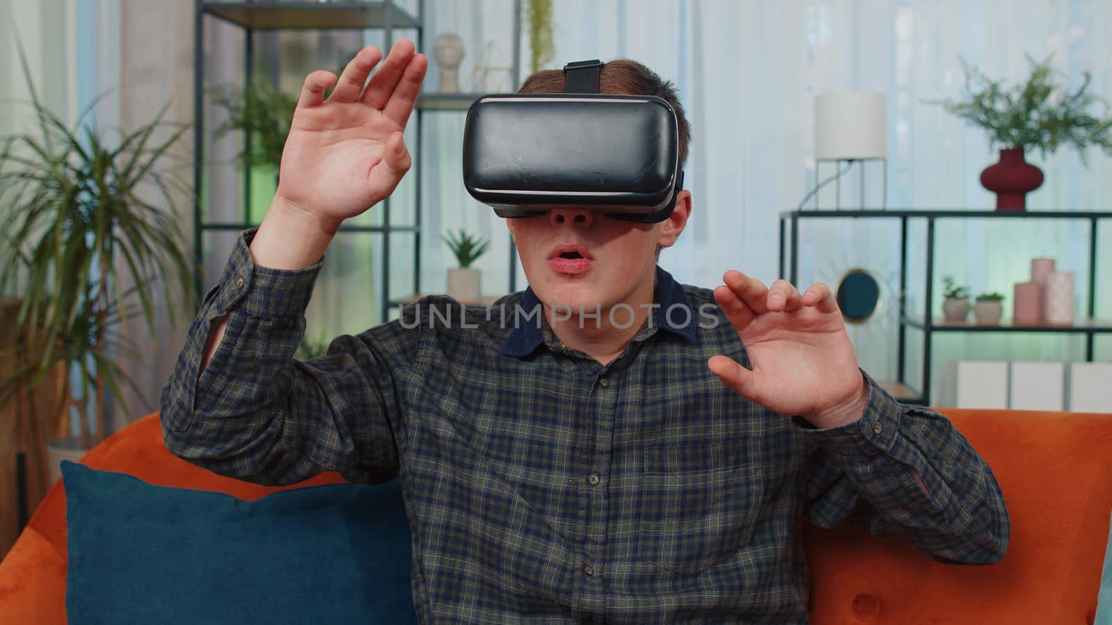 Young man boy use VR headset glasses at home, enjoying 3D 360 video concept, entertaining, in positive mood, moving hands in air, sitting on sofa in living room. Virtual reality, modern gadget device