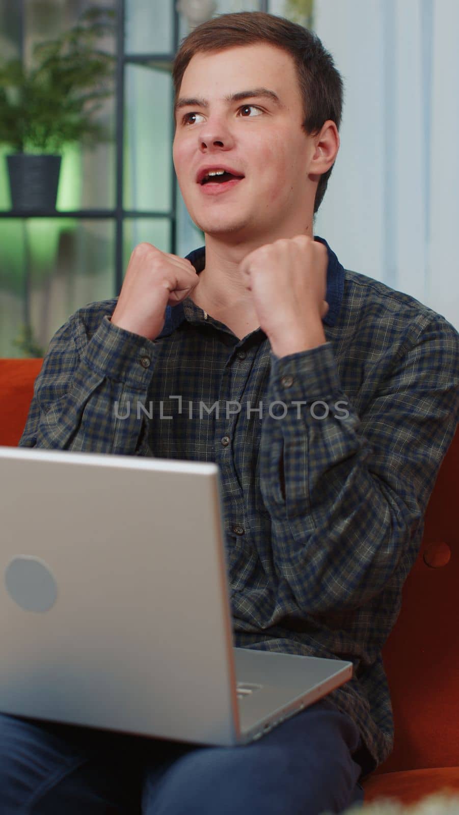 Young man use laptop computer, receive good news message, shocked by sudden victory, celebrate lottery jackpot game win, purchases online shopping at home. Vertical view shot. Amazed happy lucky guy