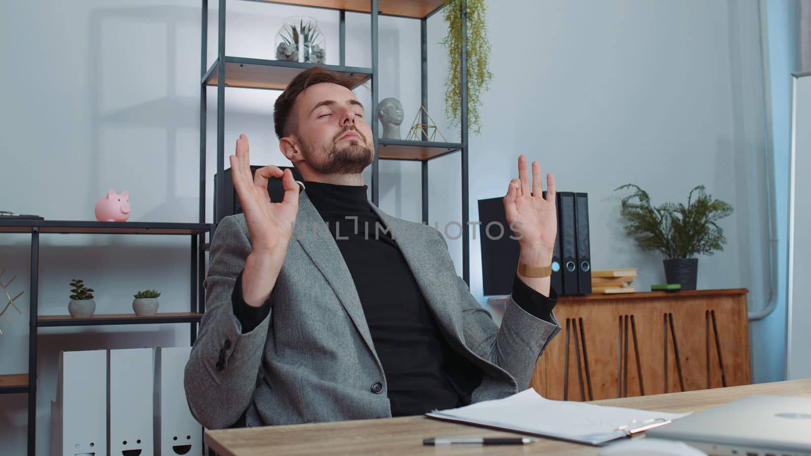 Businessman in suit working on laptop computer, meditating, doing yoga breathing exercise in lotus position at home office desk. Calm serene freelancer man taking break. Busy occupation. Peace of mind