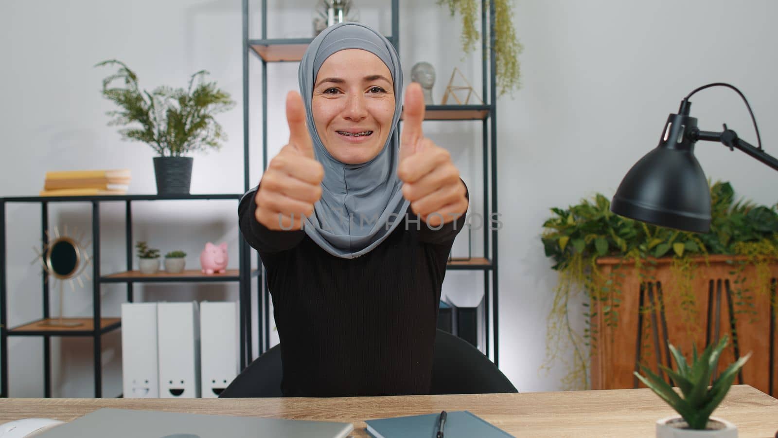 Like. Happy young muslim business woman wearing hijab headscarf looking approvingly at camera showing thumbs up, like sign positive something good, positive feedback. Girl at home office workspace