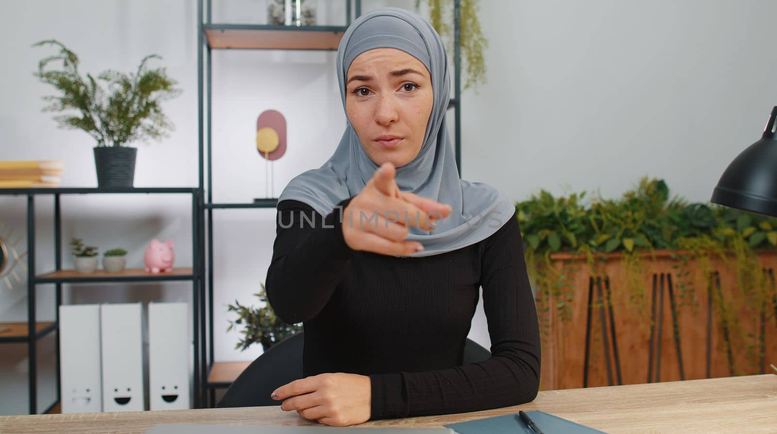 Hey you. Young muslim business woman wearing hijab smiling excitedly and pointing to camera, choosing lucky winner, indicating to awesome you, inviting, approve. Girl at modern home office workspace