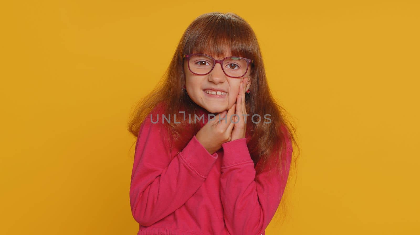 Dental problems. Young preteen child girl kid touching cheek, closing eyes with expression of terrible suffer from painful toothache, sensitive teeth, cavities. Toddler children on yellow background