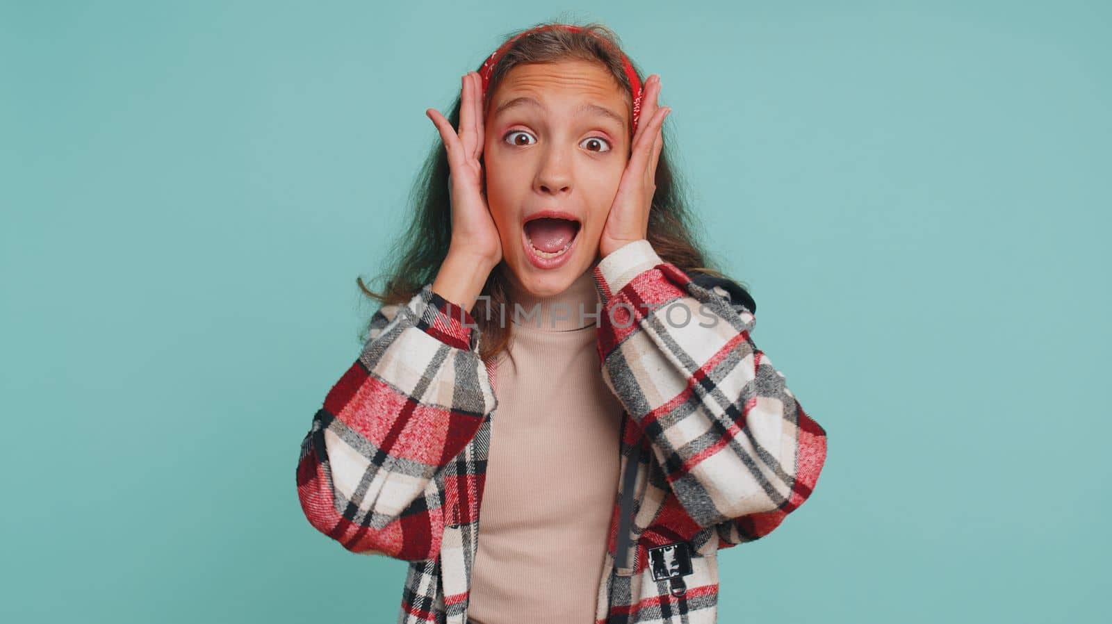 Oh my God, Wow. Young teenager child girl kid looking surprised at camera with big eyes, shocked by sudden victory, game winning lottery goal achievemen good news. Preteen children on blue background