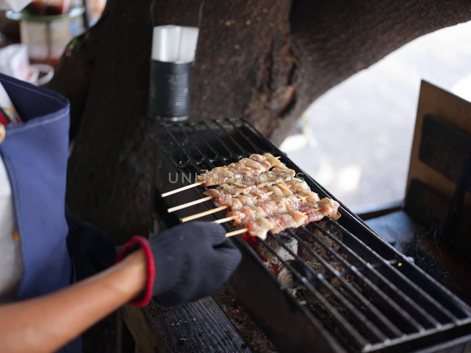 Hand holding grilled pork sticks on fire flaming in steel stove vintage style, delicious Thai street food and popular concept  .