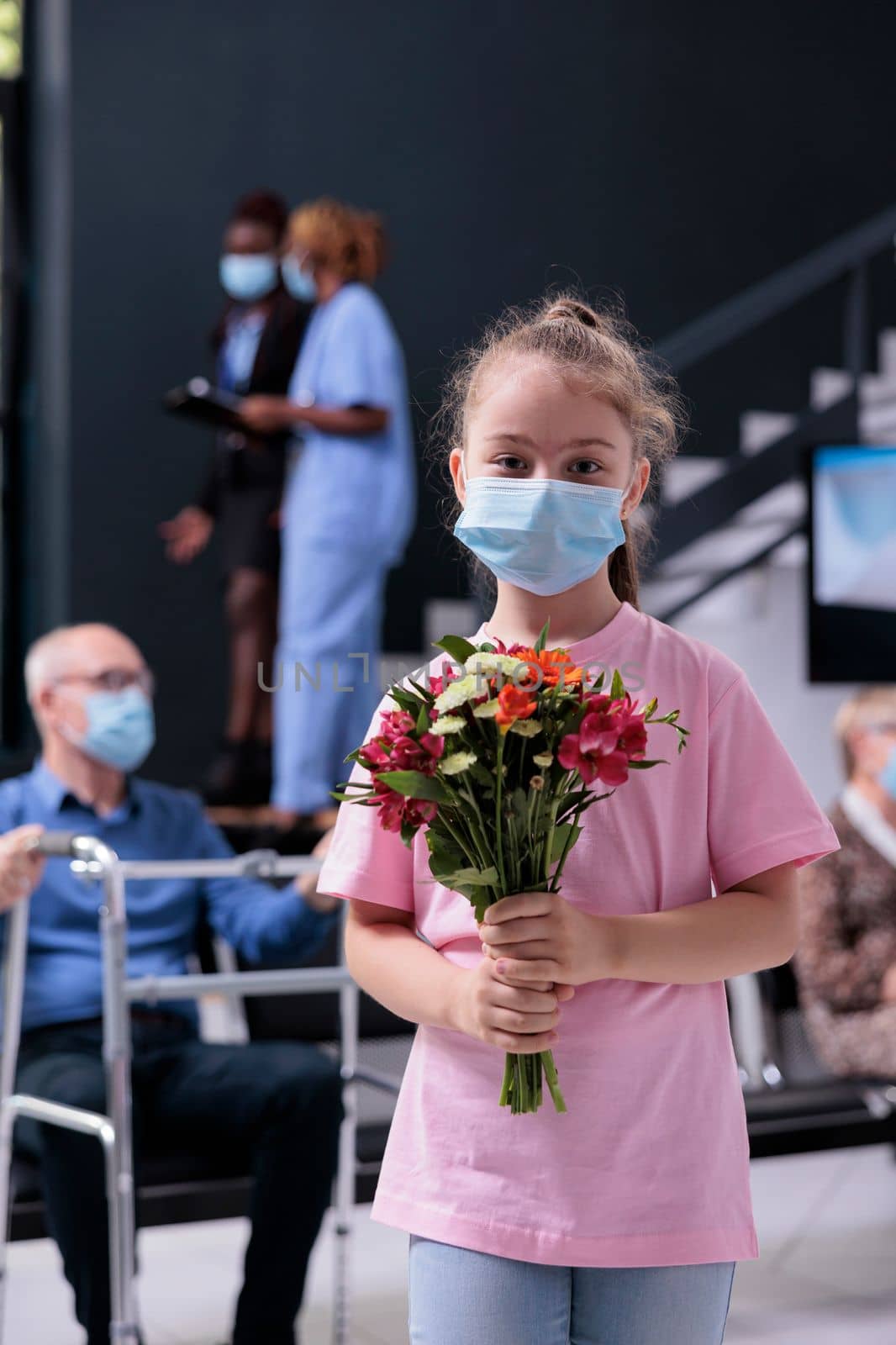 Little girl looking at camera while holding bouquet of flowers waiting for grandmother by DCStudio