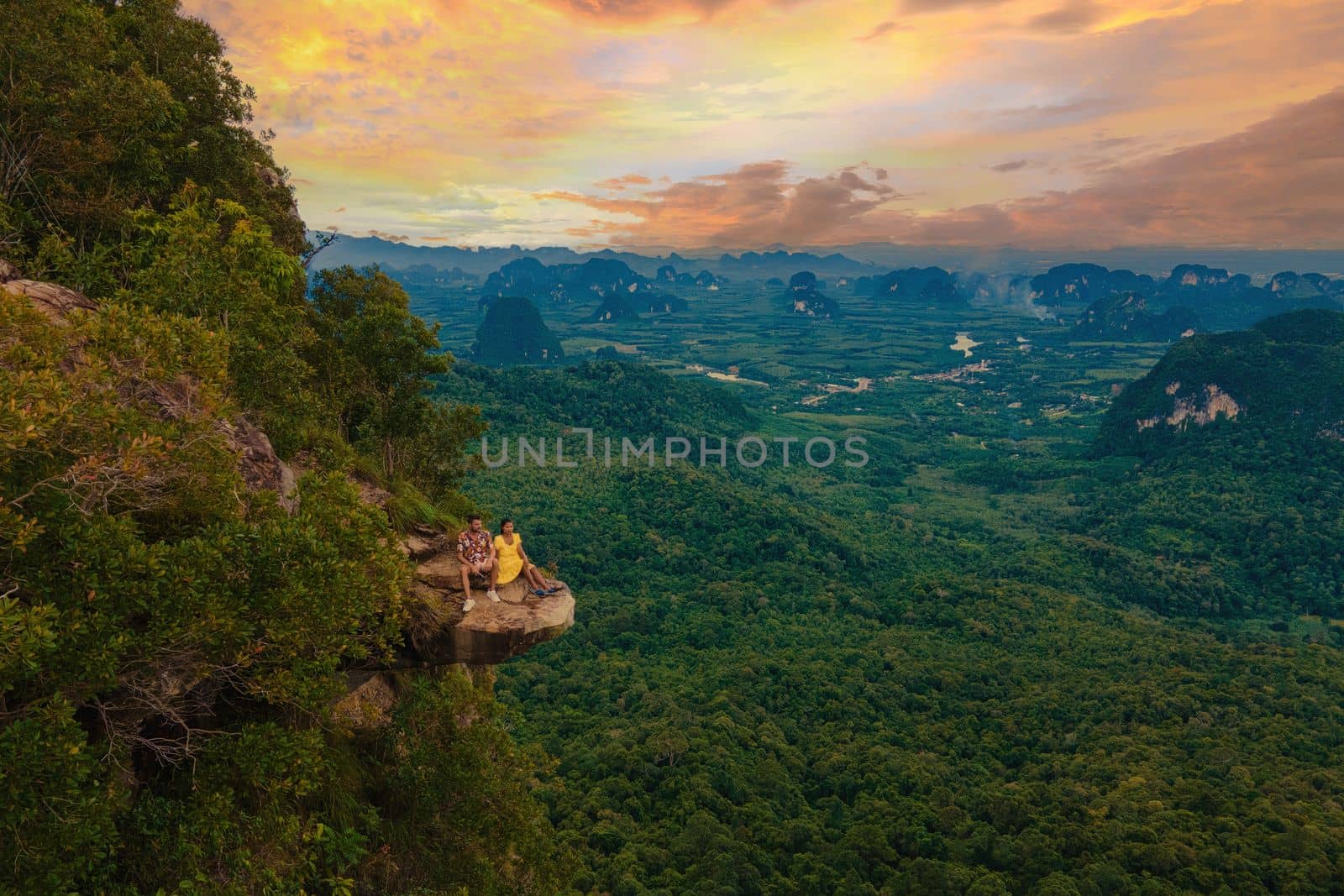 Dragon Crest mountain Krabi Thailand, a Young traveler sits on a rock that overhangs the abyss, with a beautiful landscape. Dragon Crest or Khuan Sai at Khao Ngon Nak Nature Trail in Krabi, Thailand.