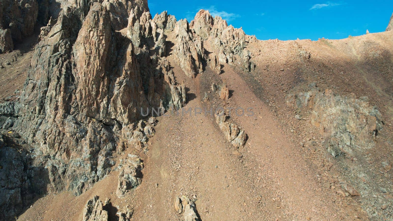 Top view of the high rocky mountains with trails. In places there is snow and yellow-orange plants grow. Shadows from clouds float on the rocks. A place to climb to the top. The mountains of Almaty