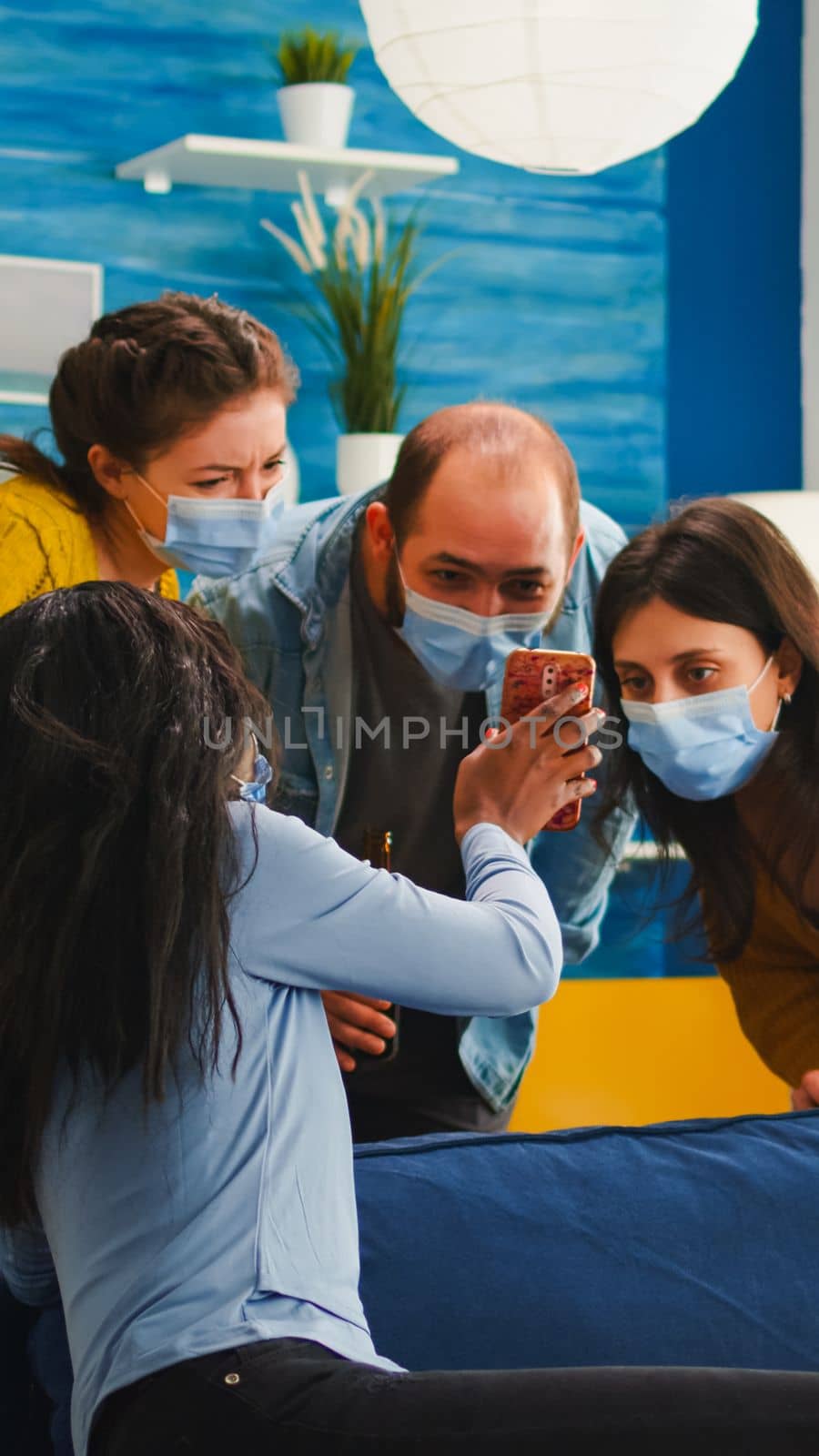 African woman showing video to friends on smartphone in living room wearing face mask as prevention against covid19 infection while hanging out. Diverse people socializing keeping social distance