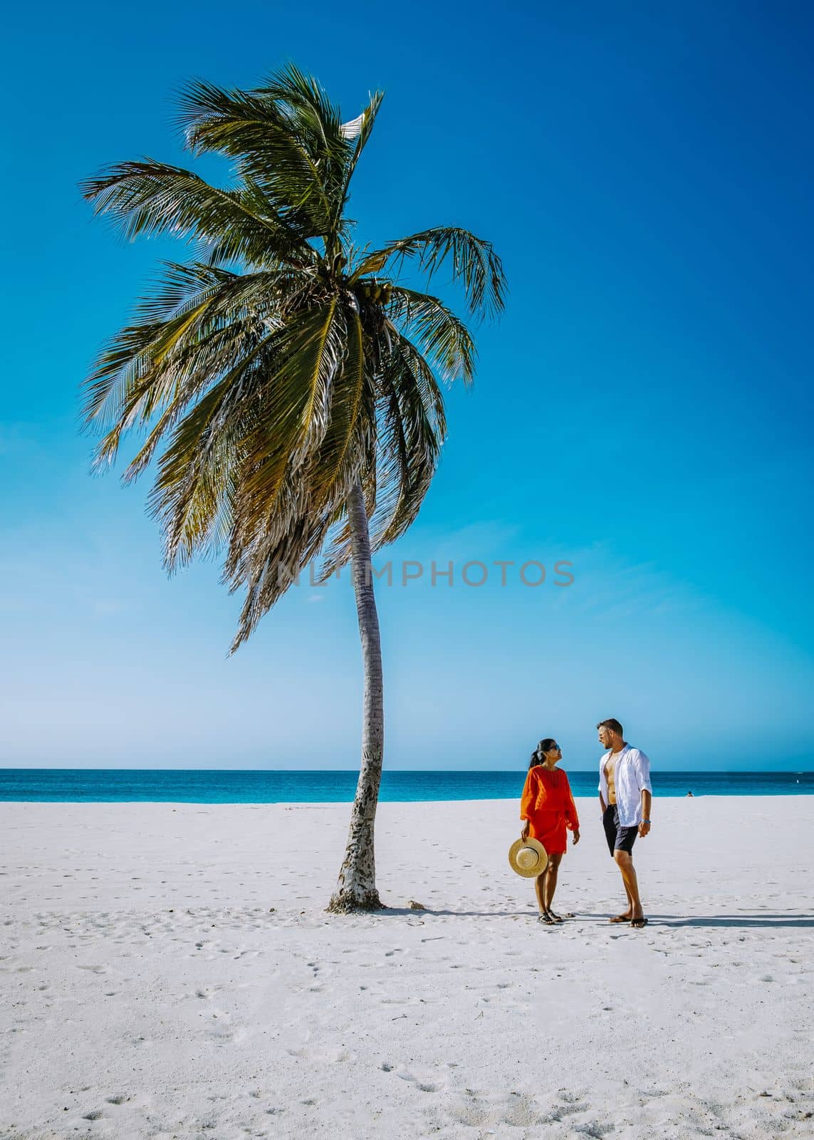 Couple walking at the beach with Palm Trees on the shoreline of Eagle Beach in Aruba by fokkebok