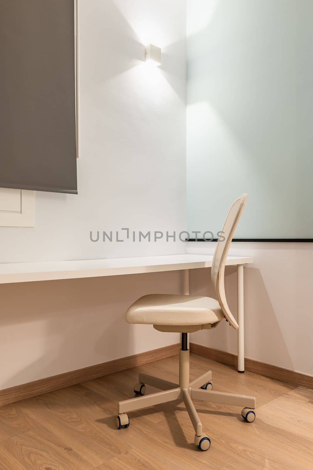 Close-up of work area with white table against wall with beige soft leather office chair for comfortable and productive work online on parquet floor. Room with bright artificial light