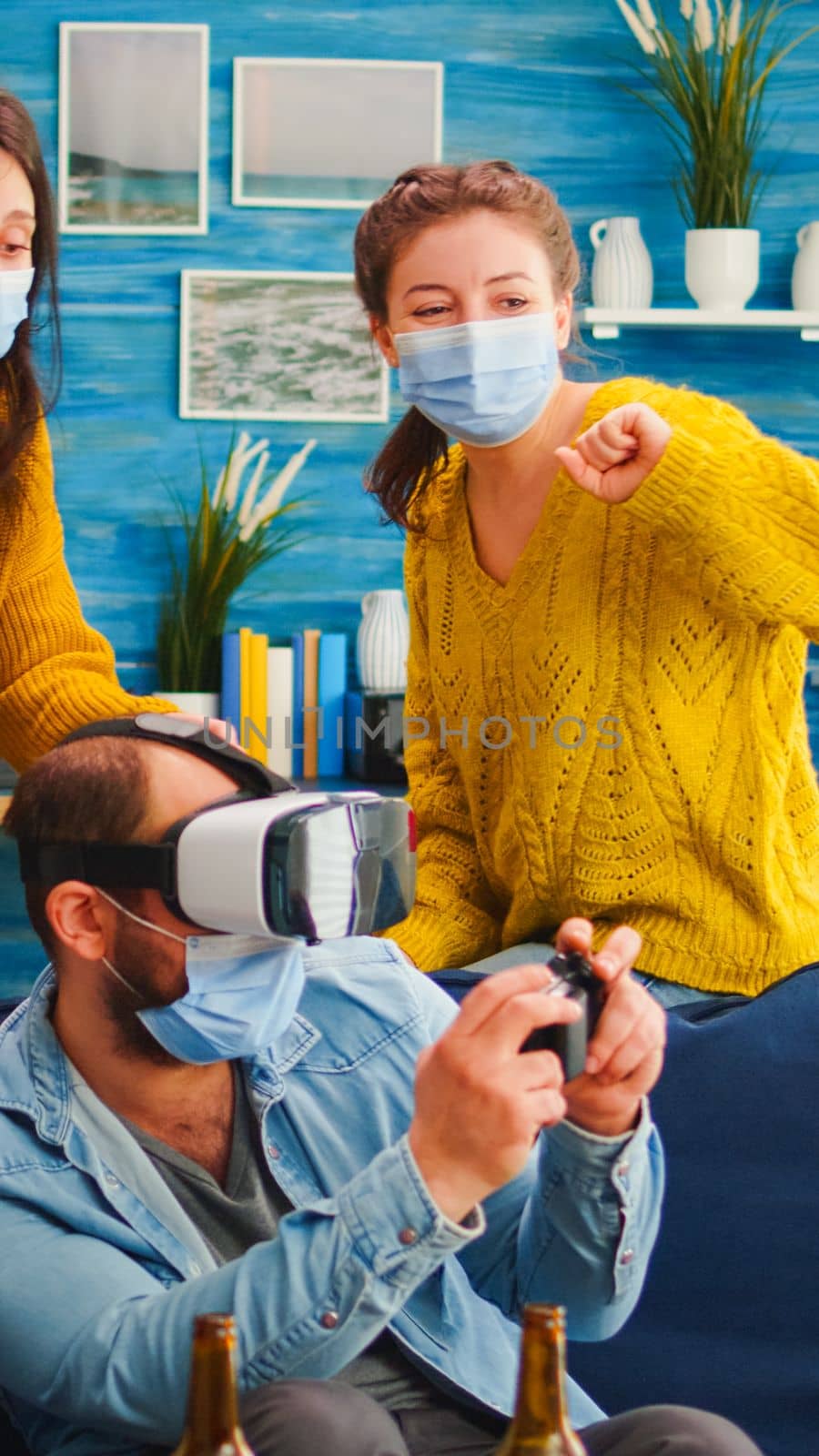 Group of multi ethnic friends with face mask enjoying playing video games using vr headset goggles in living room keeping social distancing agaist covid19. Diverse people having fun at new normal party