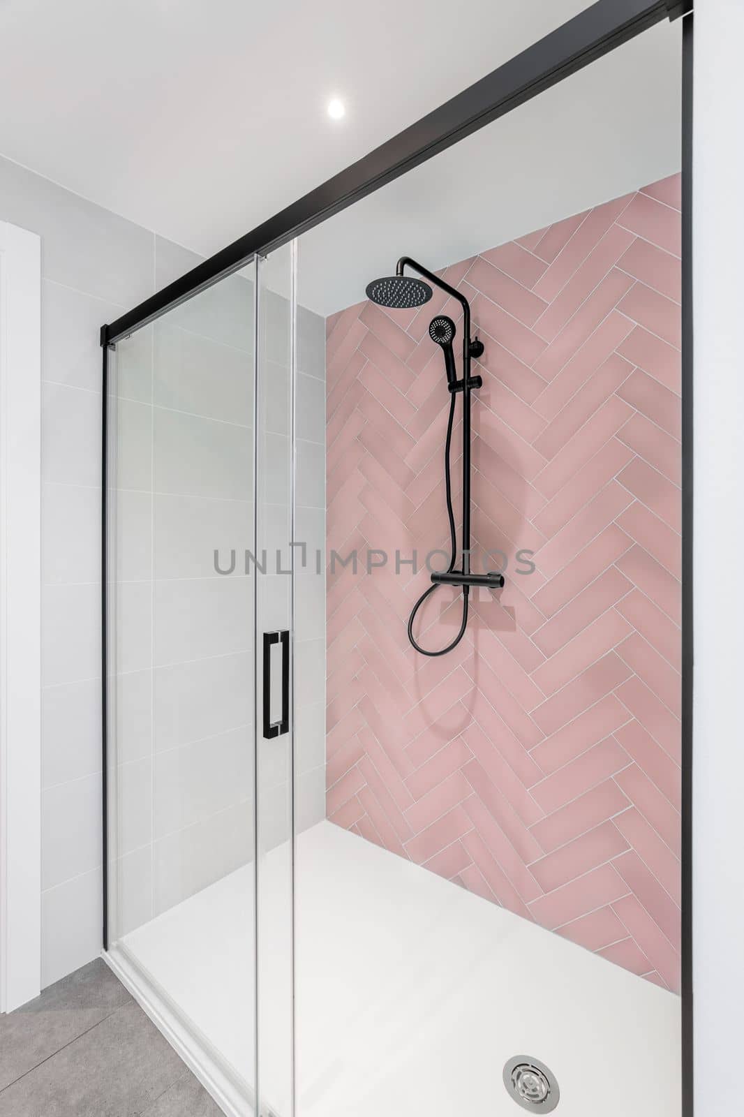 Modern bathroom with lpink and white tiles, rain head, hand held shower and glass door