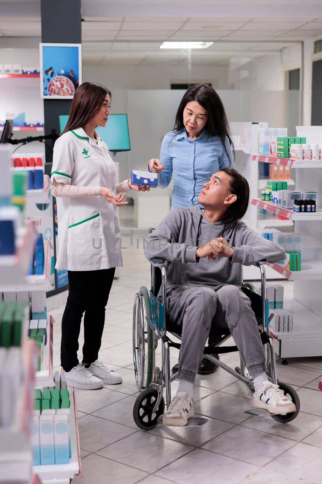 Team of asian people discussing about medication and prescription drugs, pharmacist helping man in wheelchair to buy pharmaceutical products and supplements. Client with chronic impairment.