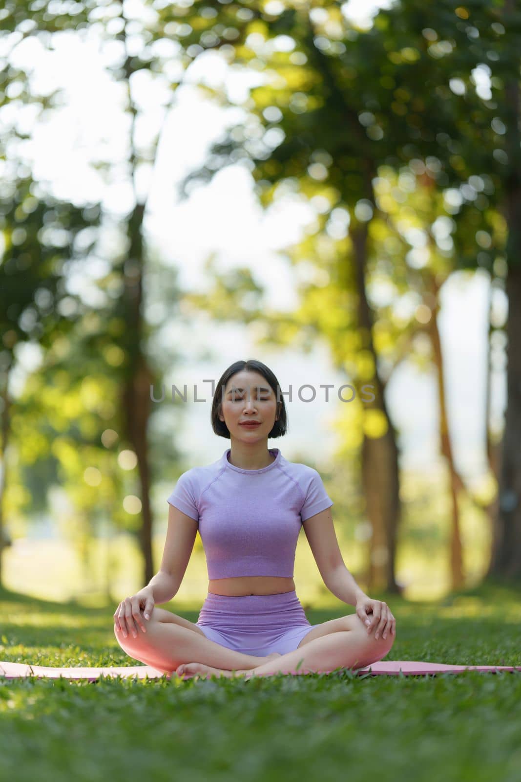 Attractive Asian woman in sportswear practicing yoga in the outdoor park.