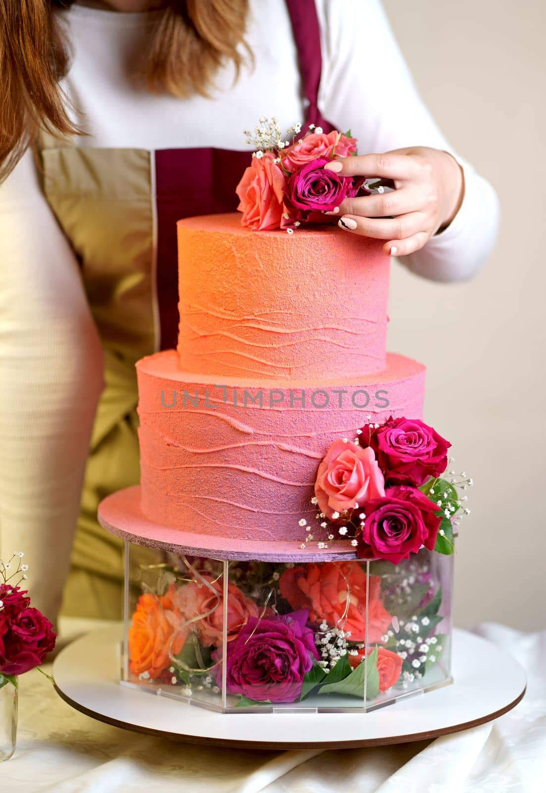 Confectioner in a working apron decorates a birthday cake with fresh flowers
