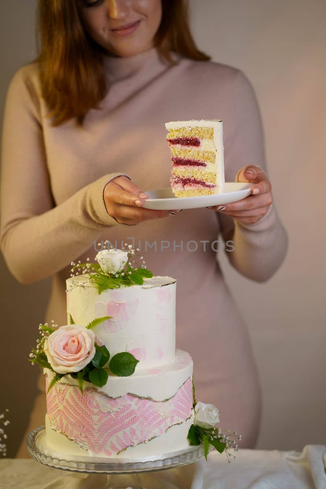 Girl cuts and serves a piece of cake. festive wedding two-tiered cake decorated with fresh flowers on a gray background by aprilphoto