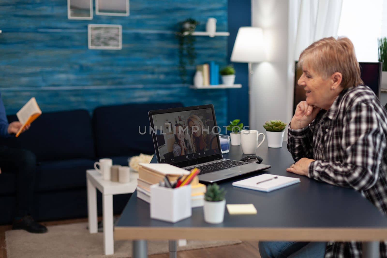 Cheerful senior woman talking with granddaughter during video conference. Happy grandmother communicating with family via online web internet video conference using modern internet technology while sitting in the living room