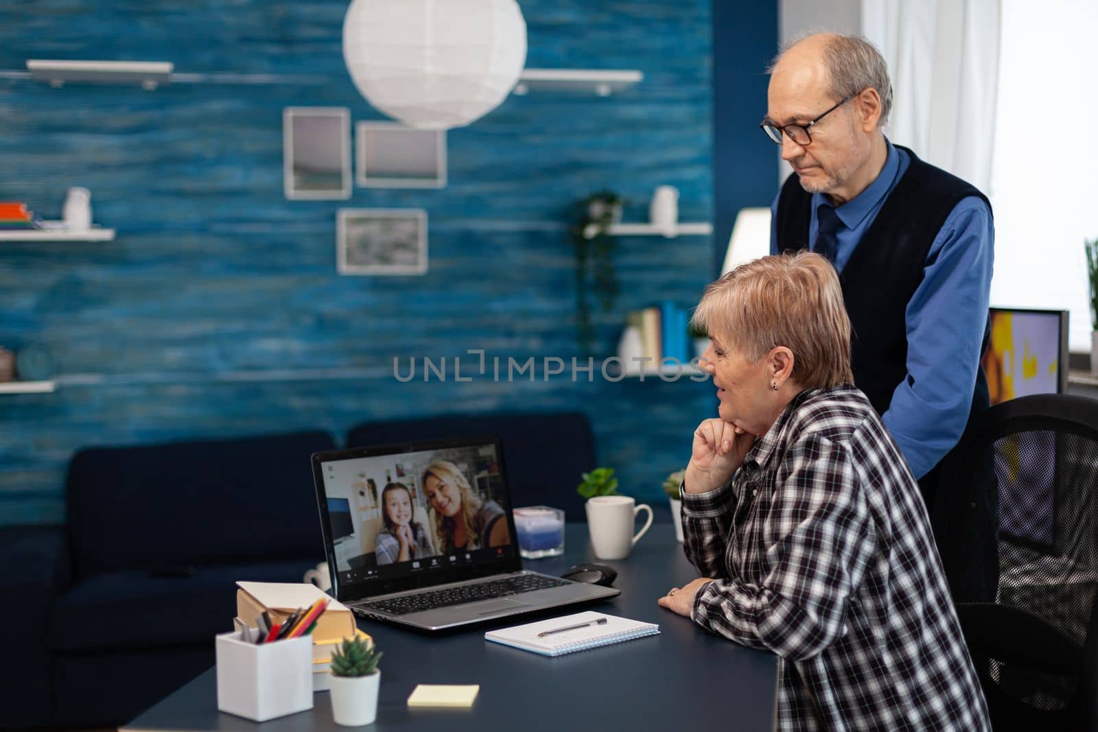 Senior man and woman talking with niece on video call. Happy grandparents communicating with family via online web internet video conference using modern internet technology while sitting in the living room