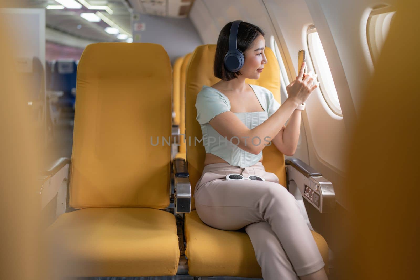 Joyful asian woman sits in the airplane and using tablet while go to travel by itchaznong