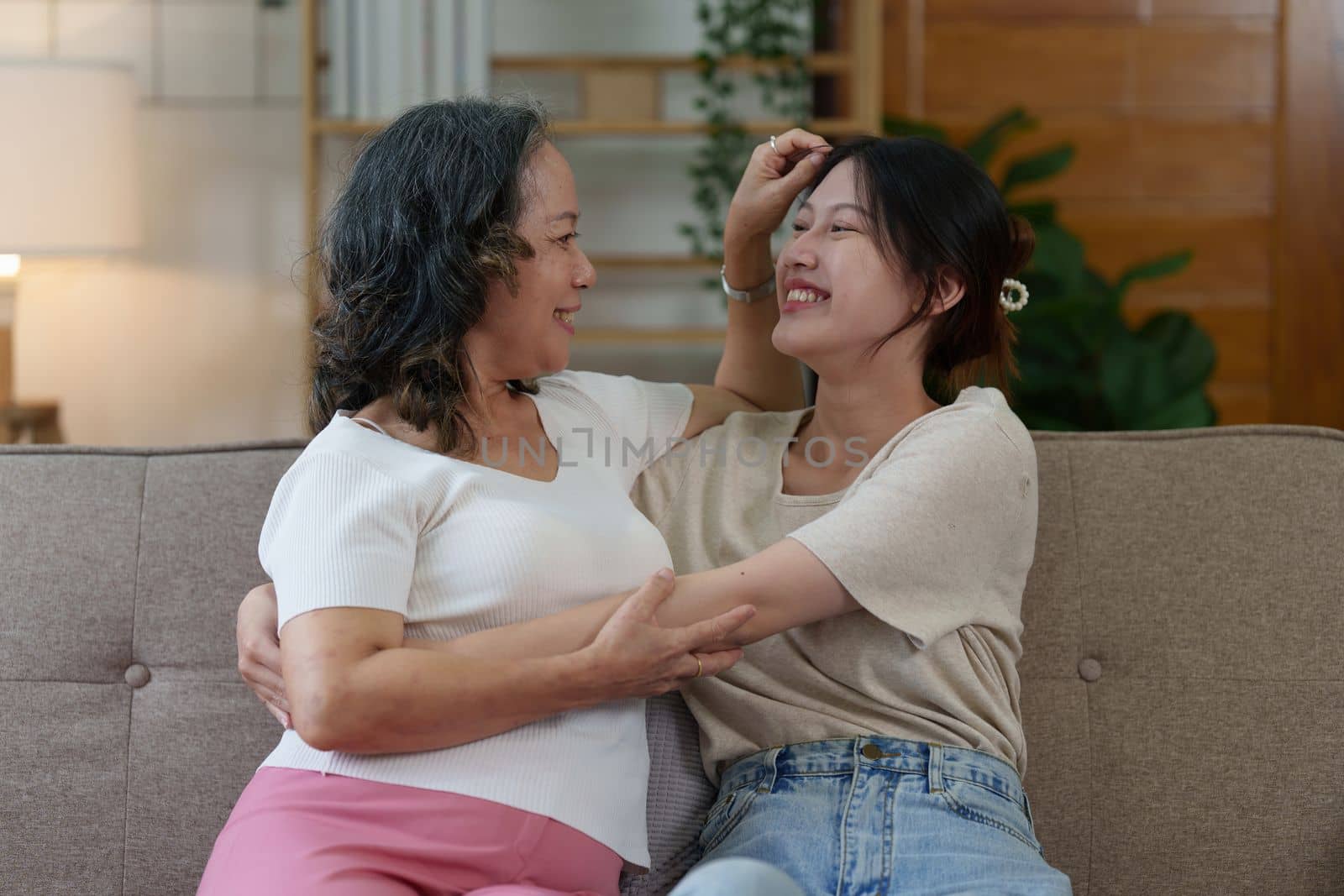 Happy senior Asian woman and her adult daughter are cuddling on the couch.