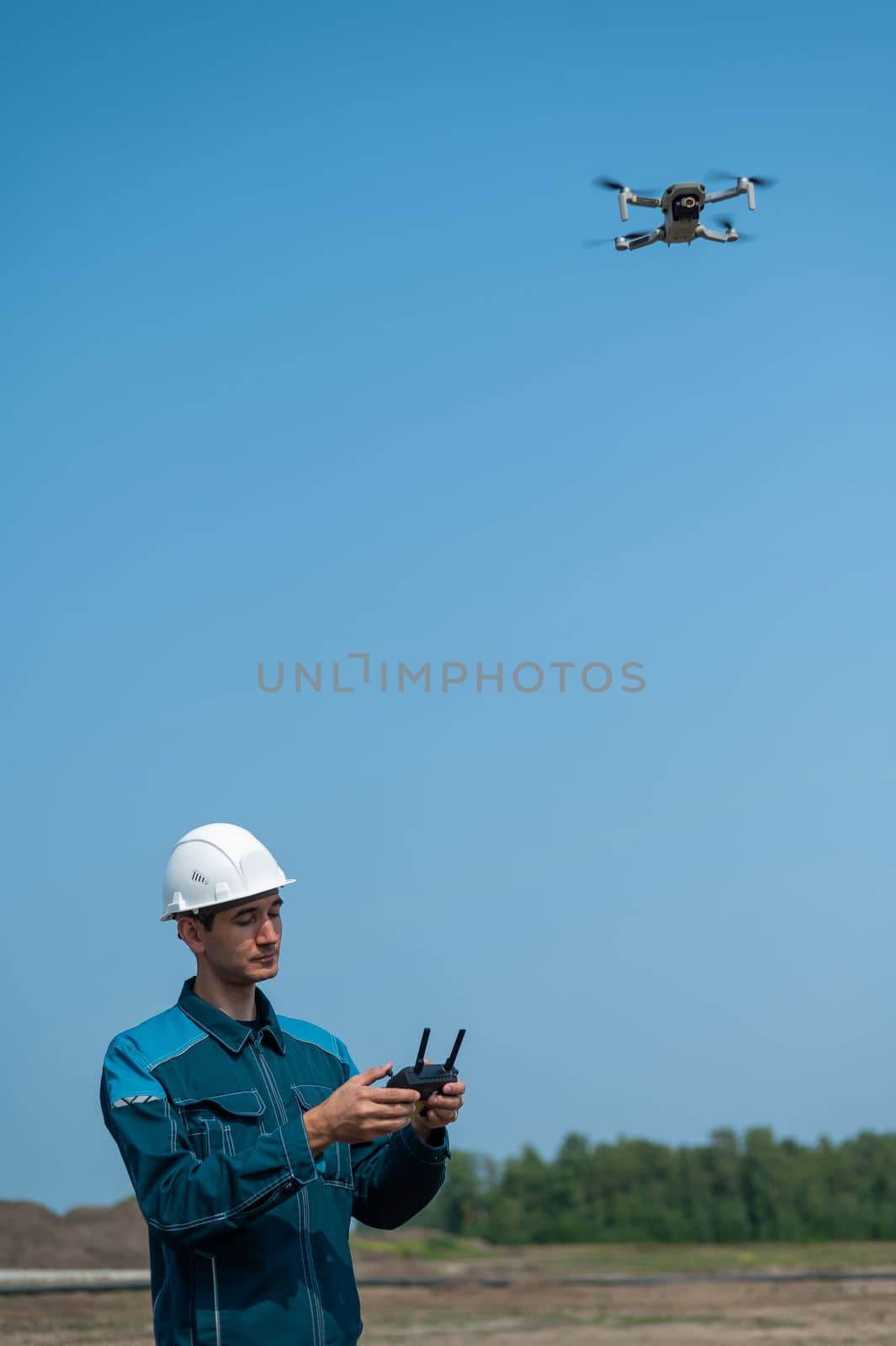 A man in a helmet and overalls controls a drone at a construction site. The builder carries out technical oversight. by mrwed54