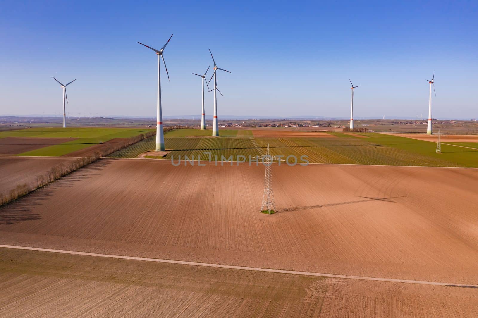 A power pole and many huge wind turbines on a field seen from above as a drone shot